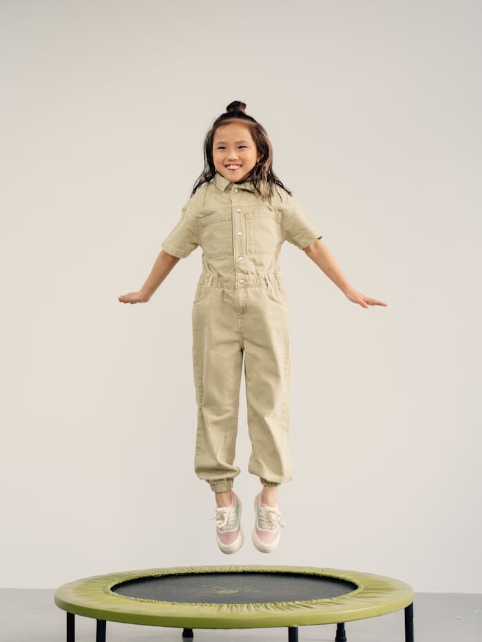 hero-img-02 Happy young girl jumping on a trampoline indoors, smiling with excitement.
